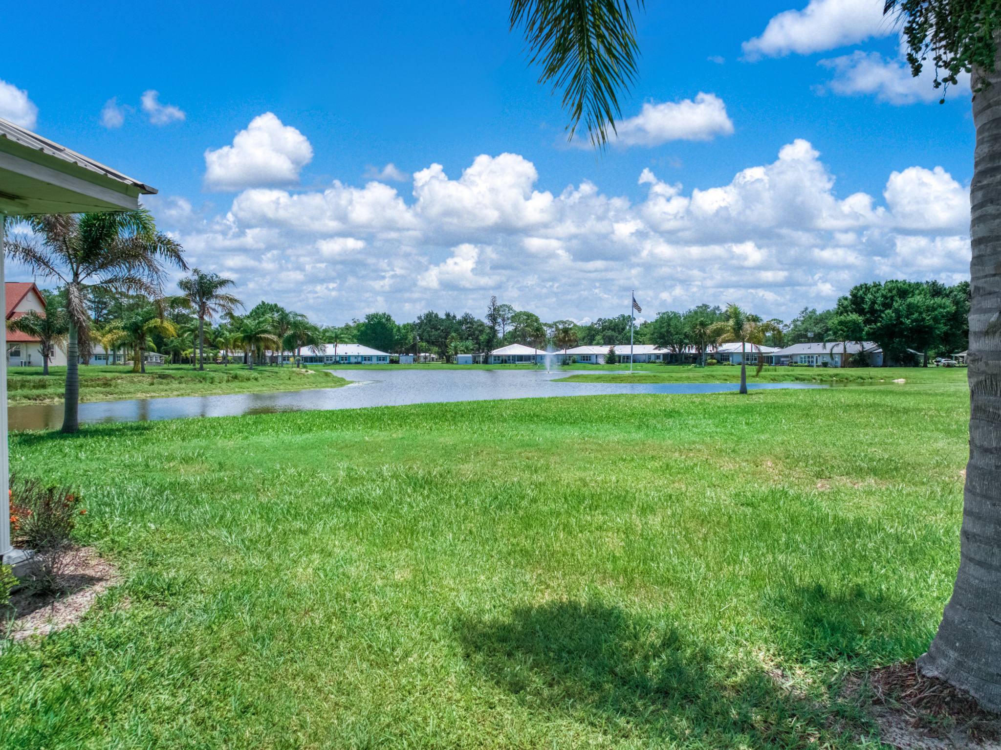 An open lawn running down to the lake, with homes and the fountain beyond